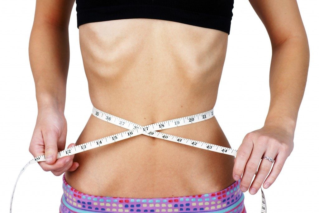 Anorexic and weight obsessed young woman, measuring her very thin and slim waist