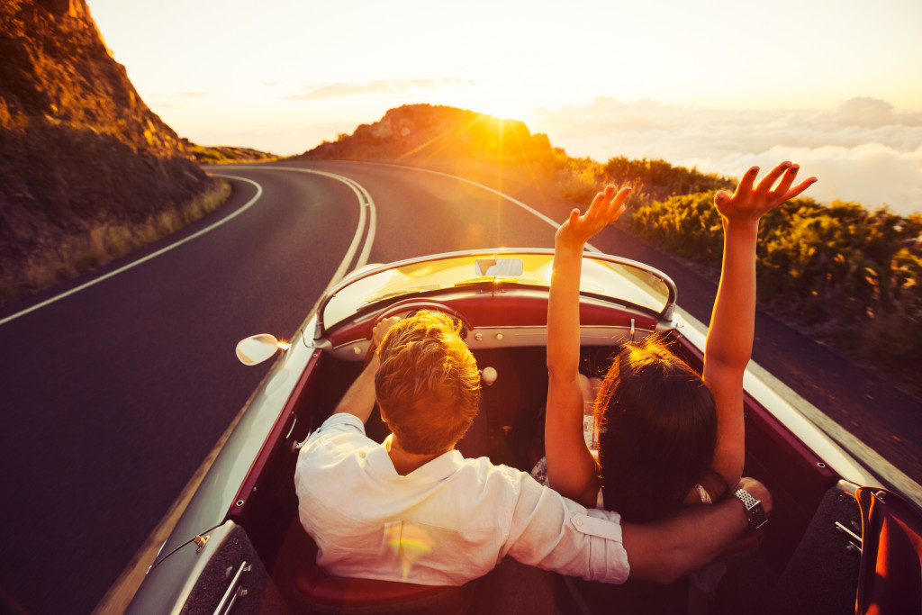 Happy Couple Driving on Country Road into the Sunset in Classic Vintage Sports Car