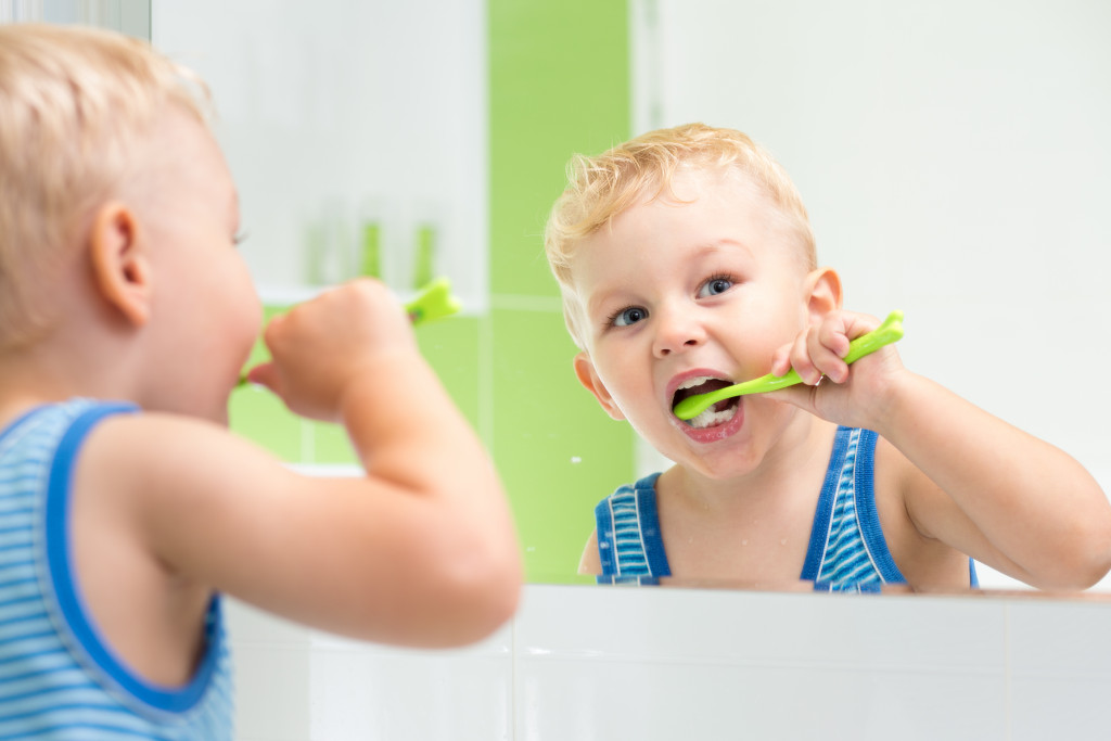A small boy looking in the mirror while brushing his teeth
